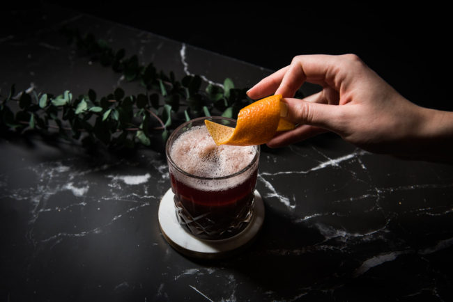 Hand placing orange peel garnish on cocktail